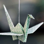 A green-patterned paper crane on a string