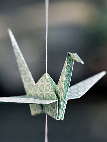 A green-patterned paper crane on a string